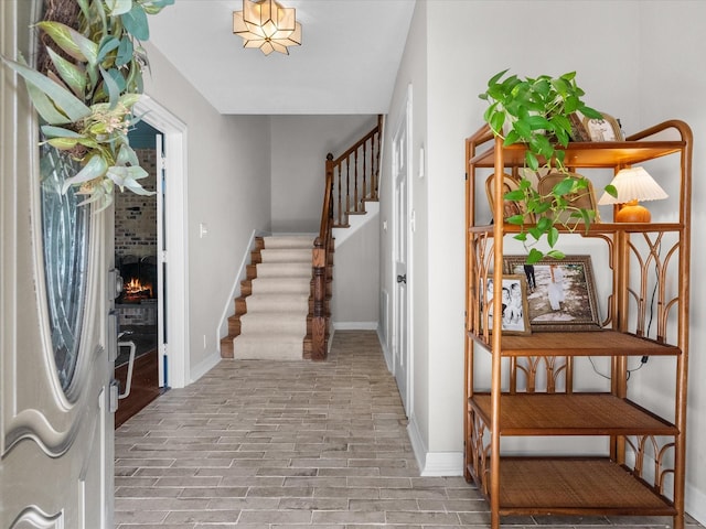 foyer featuring stairs, a brick fireplace, and baseboards