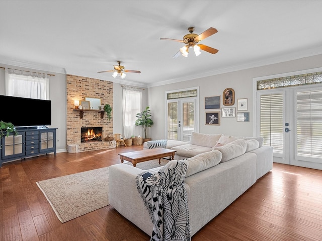 living room featuring french doors, a fireplace, wood-type flooring, ornamental molding, and a ceiling fan