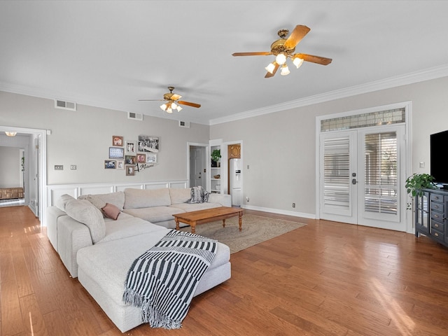 living room featuring baseboards, crown molding, visible vents, and wood finished floors