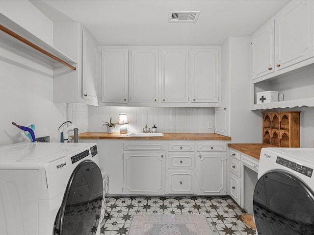 clothes washing area featuring a sink, visible vents, cabinet space, light floors, and washing machine and clothes dryer