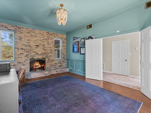 unfurnished living room with a brick fireplace, crown molding, visible vents, and wood finished floors