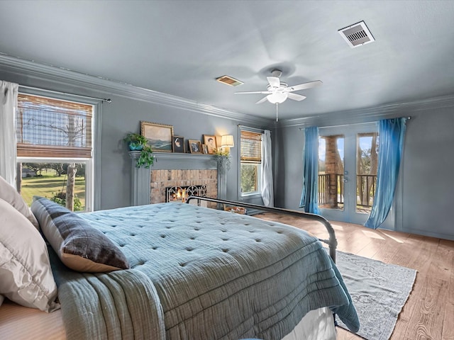 bedroom featuring access to exterior, visible vents, ornamental molding, wood finished floors, and a lit fireplace