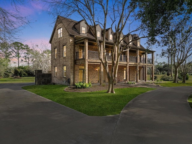 view of front of house with brick siding, a lawn, and a balcony