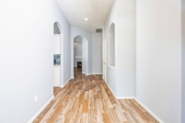 hallway featuring visible vents, light wood-style flooring, and baseboards