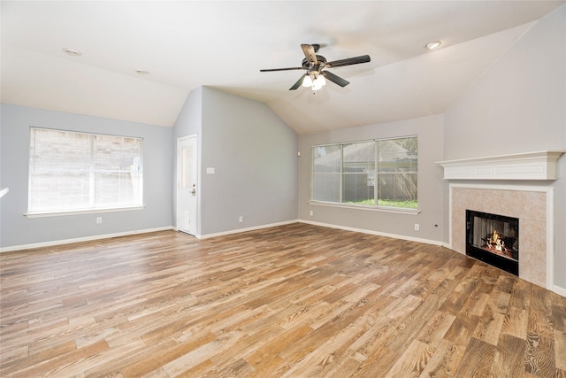 unfurnished living room with light wood-type flooring, a ceiling fan, a tiled fireplace, baseboards, and lofted ceiling