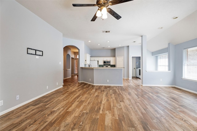 unfurnished living room with a ceiling fan, wood finished floors, visible vents, baseboards, and arched walkways