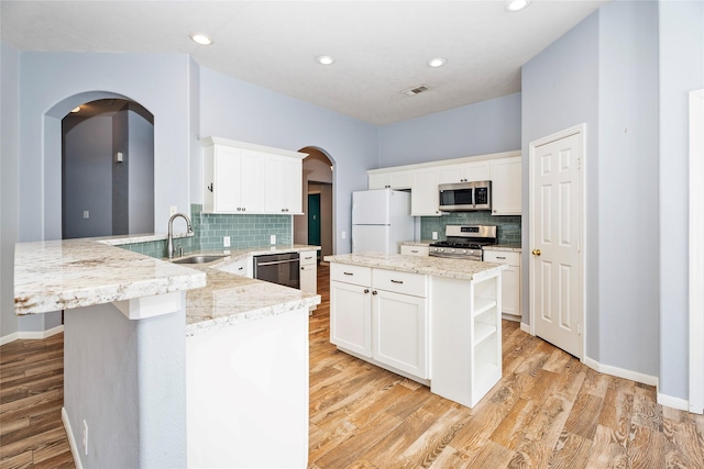 kitchen featuring visible vents, a peninsula, arched walkways, a sink, and appliances with stainless steel finishes