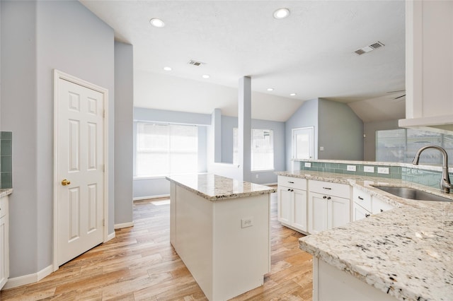 kitchen with lofted ceiling, a sink, white cabinetry, light wood finished floors, and light stone countertops