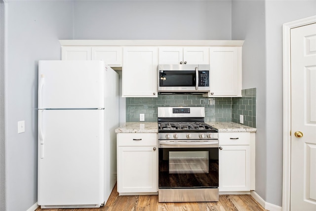 kitchen featuring light stone countertops, stainless steel appliances, decorative backsplash, white cabinets, and light wood-type flooring