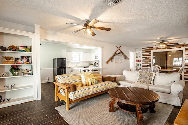 living area with a textured ceiling, dark wood-type flooring, wood walls, visible vents, and a ceiling fan