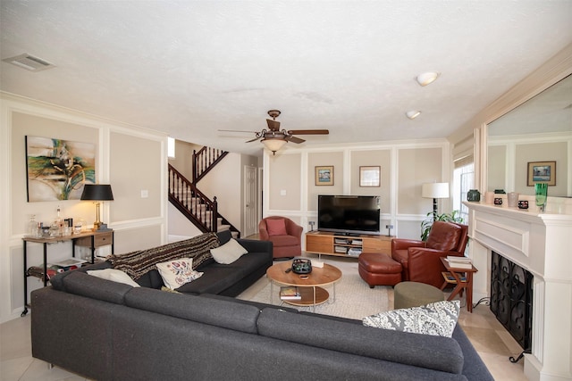 living area with a fireplace, visible vents, light tile patterned flooring, ceiling fan, and stairs