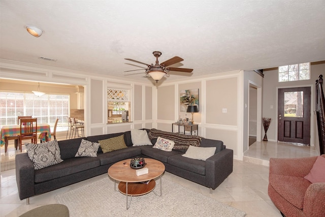 living room with ornamental molding, visible vents, a decorative wall, and ceiling fan