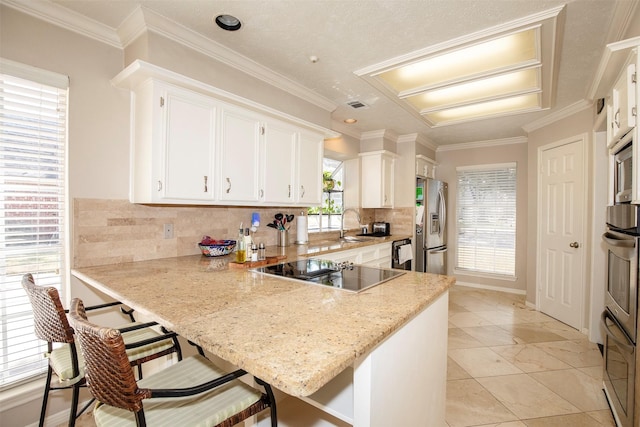 kitchen featuring a peninsula, white cabinets, backsplash, black appliances, and crown molding