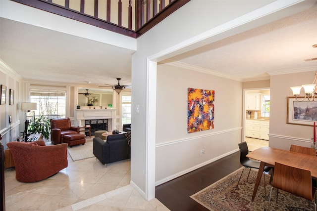 dining room featuring light tile patterned floors, baseboards, crown molding, a fireplace, and ceiling fan with notable chandelier