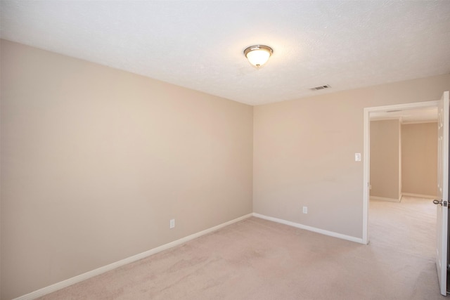 spare room featuring visible vents, light carpet, a textured ceiling, and baseboards