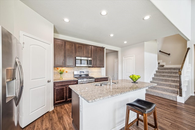 kitchen featuring light stone counters, decorative backsplash, dark wood-style floors, stainless steel appliances, and a sink