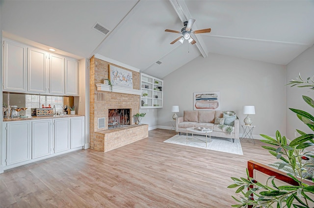 unfurnished living room featuring visible vents, light wood-style flooring, ceiling fan, vaulted ceiling with beams, and a fireplace