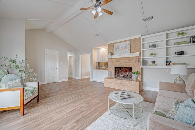living area with a fireplace, visible vents, baseboards, light wood-style floors, and beamed ceiling
