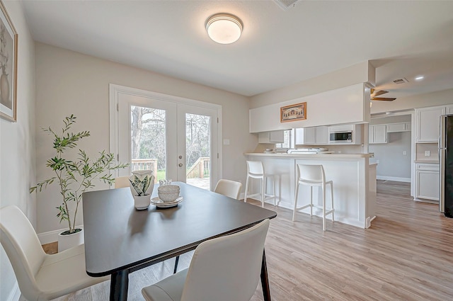 dining room featuring light wood-type flooring, french doors, visible vents, and baseboards