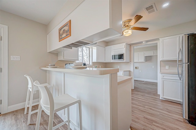 kitchen with stainless steel appliances, light countertops, visible vents, a peninsula, and a kitchen bar