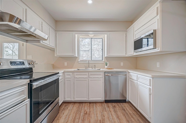 kitchen with wall chimney exhaust hood, stainless steel appliances, light wood-style floors, white cabinetry, and a sink