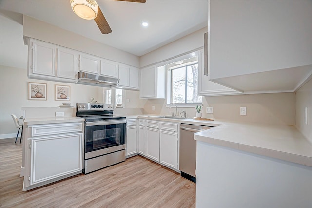 kitchen with light wood finished floors, appliances with stainless steel finishes, white cabinets, a sink, and under cabinet range hood