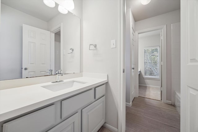 bathroom with a tub, vanity, baseboards, and wood finished floors