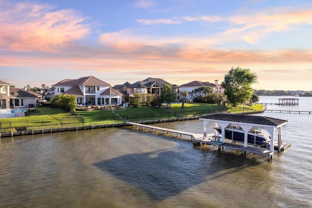 dock area featuring boat lift, a water view, fence, a lawn, and a residential view