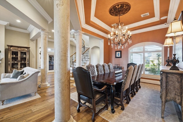 dining room with wood finished floors, visible vents, stairway, a tray ceiling, and decorative columns