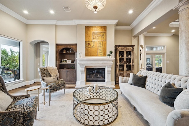 living room featuring light wood finished floors, visible vents, arched walkways, a glass covered fireplace, and built in shelves