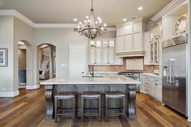 kitchen with arched walkways, a sink, tasteful backsplash, high end appliances, and an island with sink