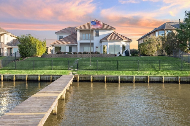 dock area with a lawn, a water view, a fenced backyard, and a balcony