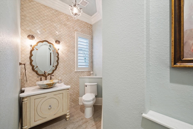 bathroom featuring a textured wall, crown molding, vanity, and toilet