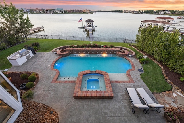 pool at dusk featuring a patio, a pool with connected hot tub, a water view, a lawn, and a fenced backyard