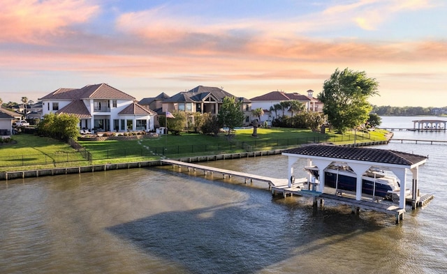 dock area featuring a water view, a lawn, boat lift, and a fenced backyard