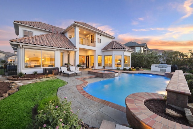 back of property at dusk with exterior kitchen, a tile roof, fence, and a balcony