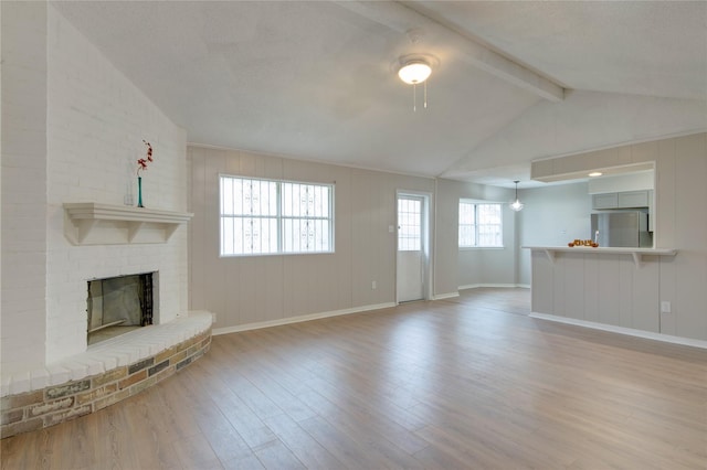 unfurnished living room featuring lofted ceiling with beams, a brick fireplace, wood finished floors, and baseboards