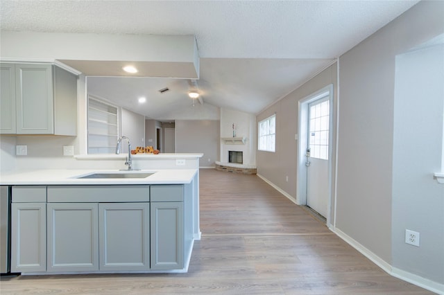 kitchen with gray cabinetry, a peninsula, a sink, vaulted ceiling, and light wood-type flooring