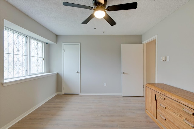 unfurnished bedroom with a textured ceiling, light wood-type flooring, a ceiling fan, and baseboards