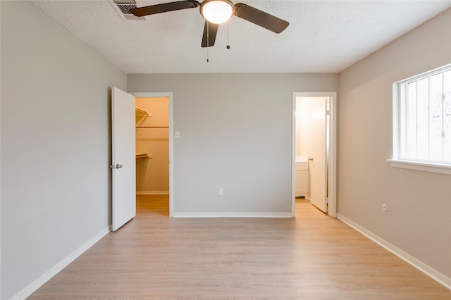 unfurnished bedroom featuring light wood-style floors, a spacious closet, visible vents, and a textured ceiling