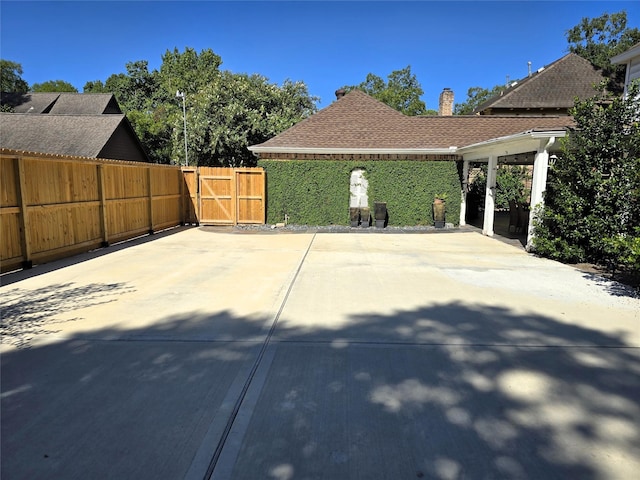 view of side of home featuring a shingled roof, a gate, a patio, and fence