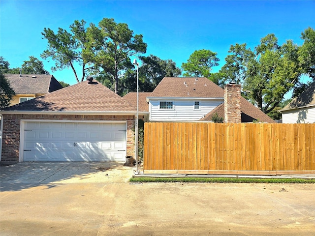 view of front of home featuring driveway, a chimney, an attached garage, and fence