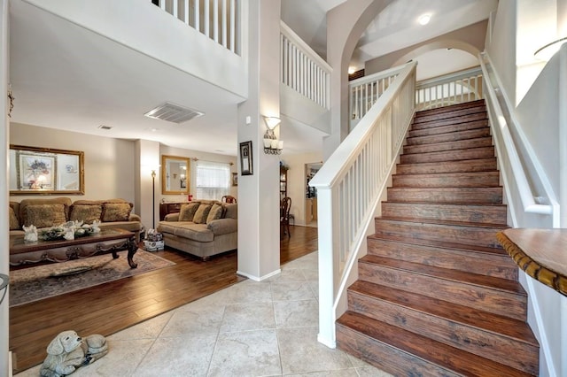 stairway with baseboards, visible vents, a high ceiling, and wood finished floors