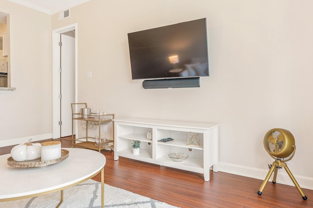 living area featuring baseboards, visible vents, wood finished floors, and ornamental molding