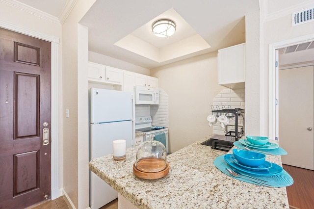 kitchen featuring white appliances, visible vents, white cabinets, a raised ceiling, and a sink