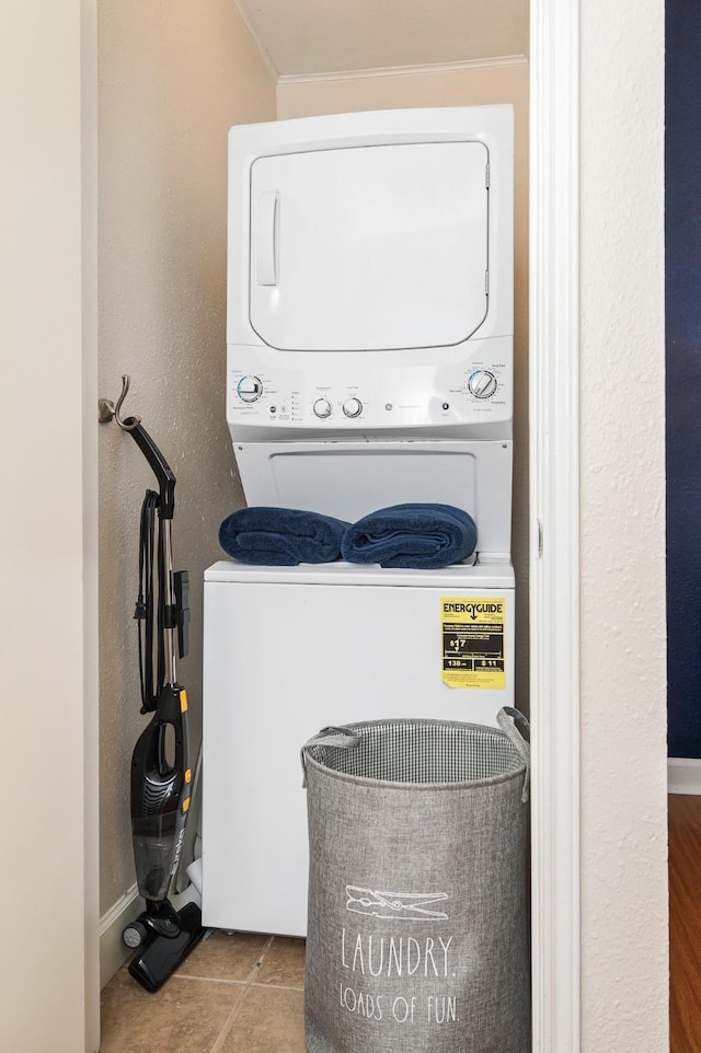 washroom featuring laundry area, tile patterned flooring, stacked washer and clothes dryer, and crown molding