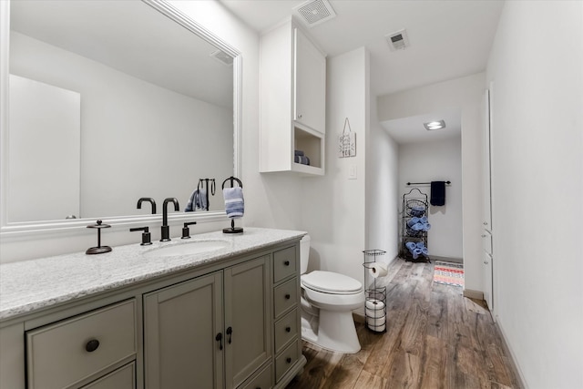 bathroom with toilet, vanity, wood finished floors, and visible vents