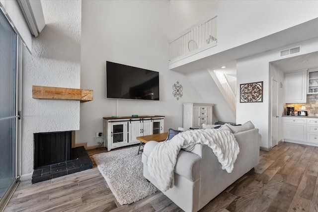 living room featuring visible vents, a fireplace with raised hearth, a towering ceiling, wood finished floors, and baseboards