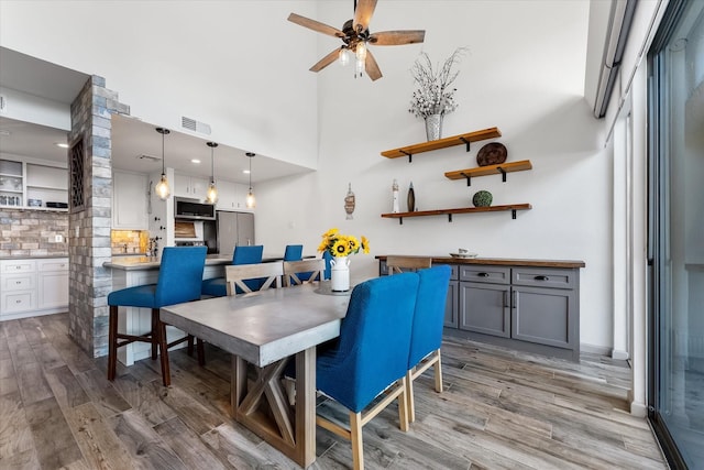 dining area with light wood-style flooring, a high ceiling, visible vents, and ceiling fan