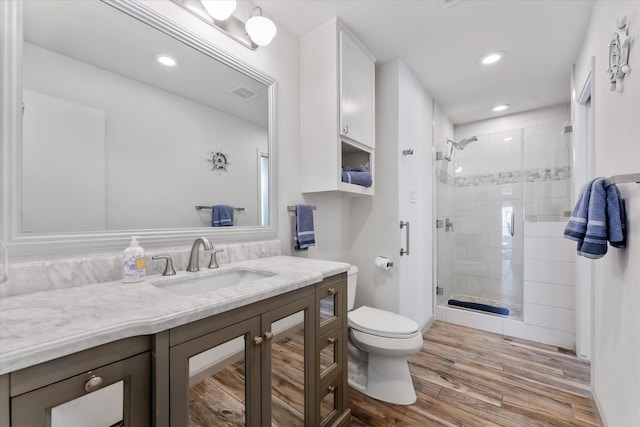 bathroom with visible vents, toilet, vanity, a shower stall, and wood finished floors